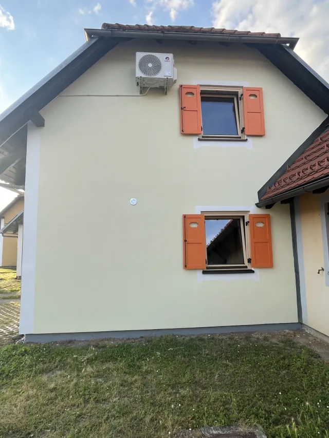 Zunanjost hiške s klimatsko napravo in zelenico